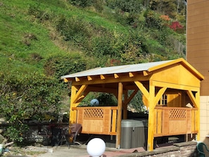 A wooden gazebo with a sloped roof, a trash bin, and a table with chairs.