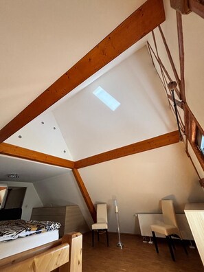 A room with a sloped ceiling, wooden beams, a skylight, two chairs, a floor lamp, and a bed with a patterned blanket. - Landgasthof Kleine Kommode (Walkenried)