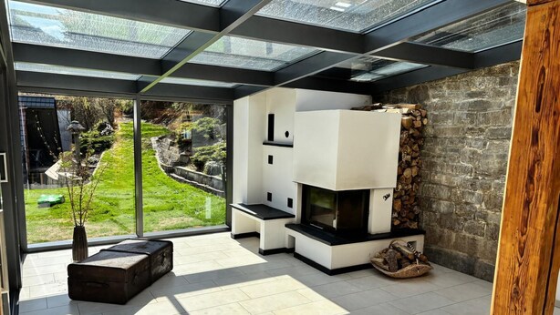 A modern living room with a fireplace, large windows, and a view of a garden. - Landgasthof Kleine Kommode (Walkenried)