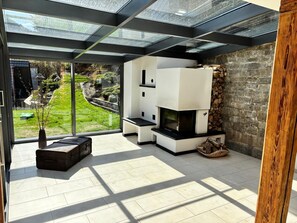 Ein modernes Wohnzimmer mit Kamin, großen Fenstern und Blick auf einen Garten.