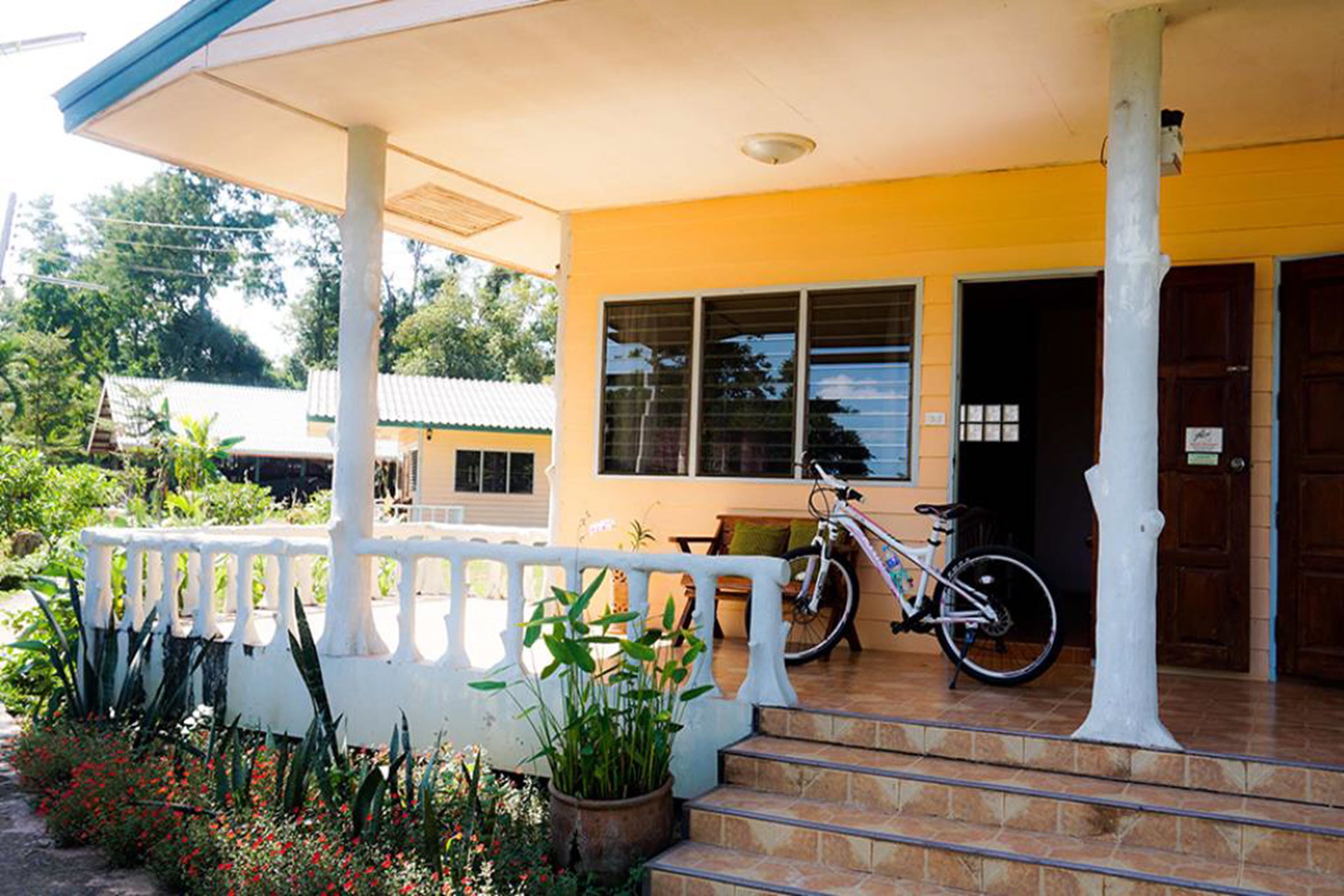 A building with a yellow exterior, a covered porch with a white railing, and a bicycle parked on the steps.