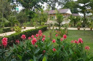 Um jardim exuberante com flores cor-de-rosa e um edifício com telhado de azulejos.