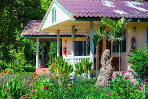 Uma casa com telhado de cerâmica, varanda e jardim com diversas plantas e flores.