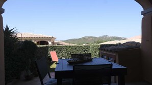 Une terrasse extérieure avec une table et des chaises, une vue sur un bâtiment avec un toit en tuiles et un paysage montagneux en arrière-plan.