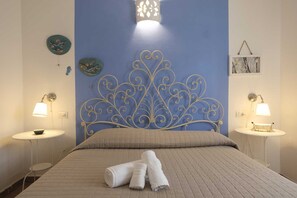 A bedroom with a blue accent wall, a decorative metal headboard, two bedside tables with lamps, and a neatly made bed with rolled towels.