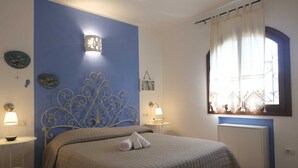 Une chambre avec un mur d’accent bleu, une tête de lit décorative, une fenêtre avec des rideaux et des lampes de chevet.