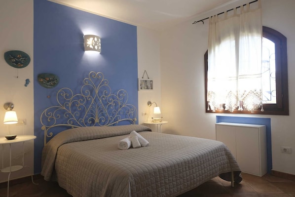 A bedroom with a blue accent wall, a decorative headboard, a window with curtains, and bedside lamps.