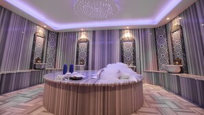 Une salle de spa luxueuse, dotée d’une table ronde en bois, de panneaux muraux décoratifs et d’un plafond agrémenté d’un luminaire représentant un ciel étoilé.