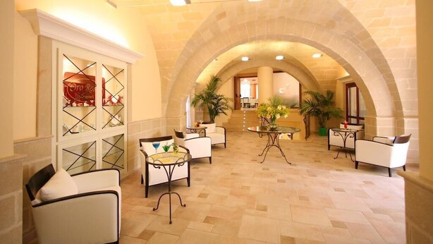 Un hall d’entrée spacieux avec un plafond haut, une architecture en pierre avec des arches, et de nombreux espaces de détente dotés de tables et de chaises.