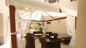 Un espace extérieur abrité, aménagé avec des meubles en osier et surmonté d’un auvent.