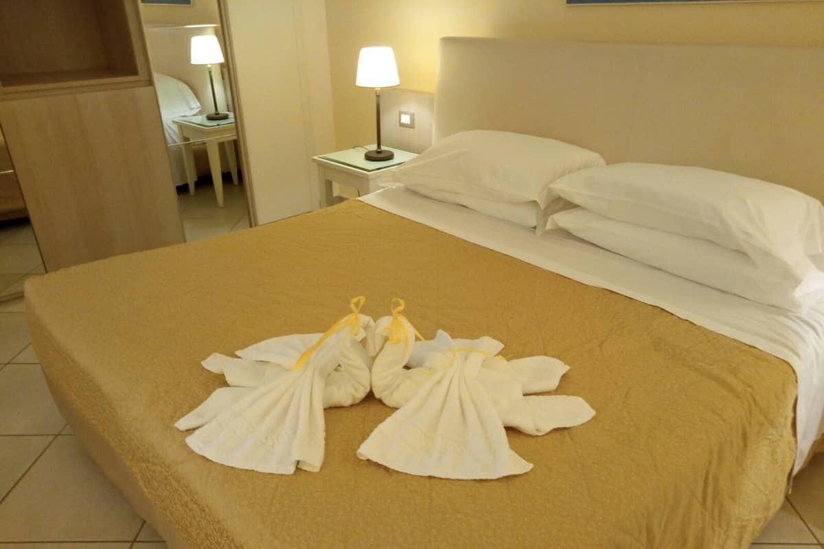 A hotel room with a neatly made bed, a bedside table with a lamp, and a mirror.
