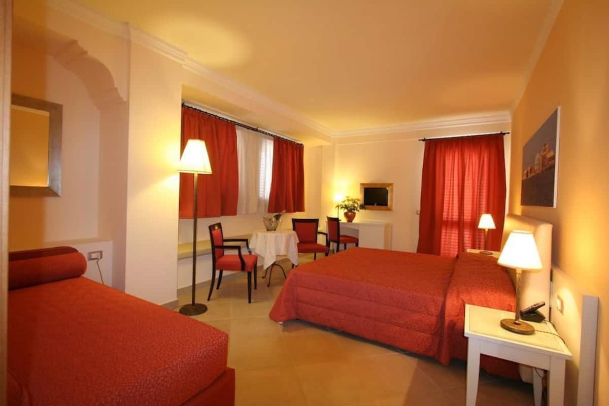A hotel room with two beds, a desk, chairs, a TV, and a lamp.