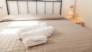 A bed with a quilted beige bedspread, two neatly folded white towels, and a bedside table with a lamp. - Aria di vacanza - Borgo Turchese (Olbia)