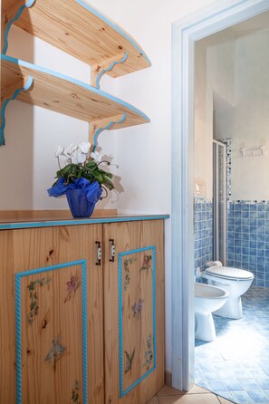 Et badeværelse med en trækommode, et bruseområde med blå fliser og et hvidt toilet.