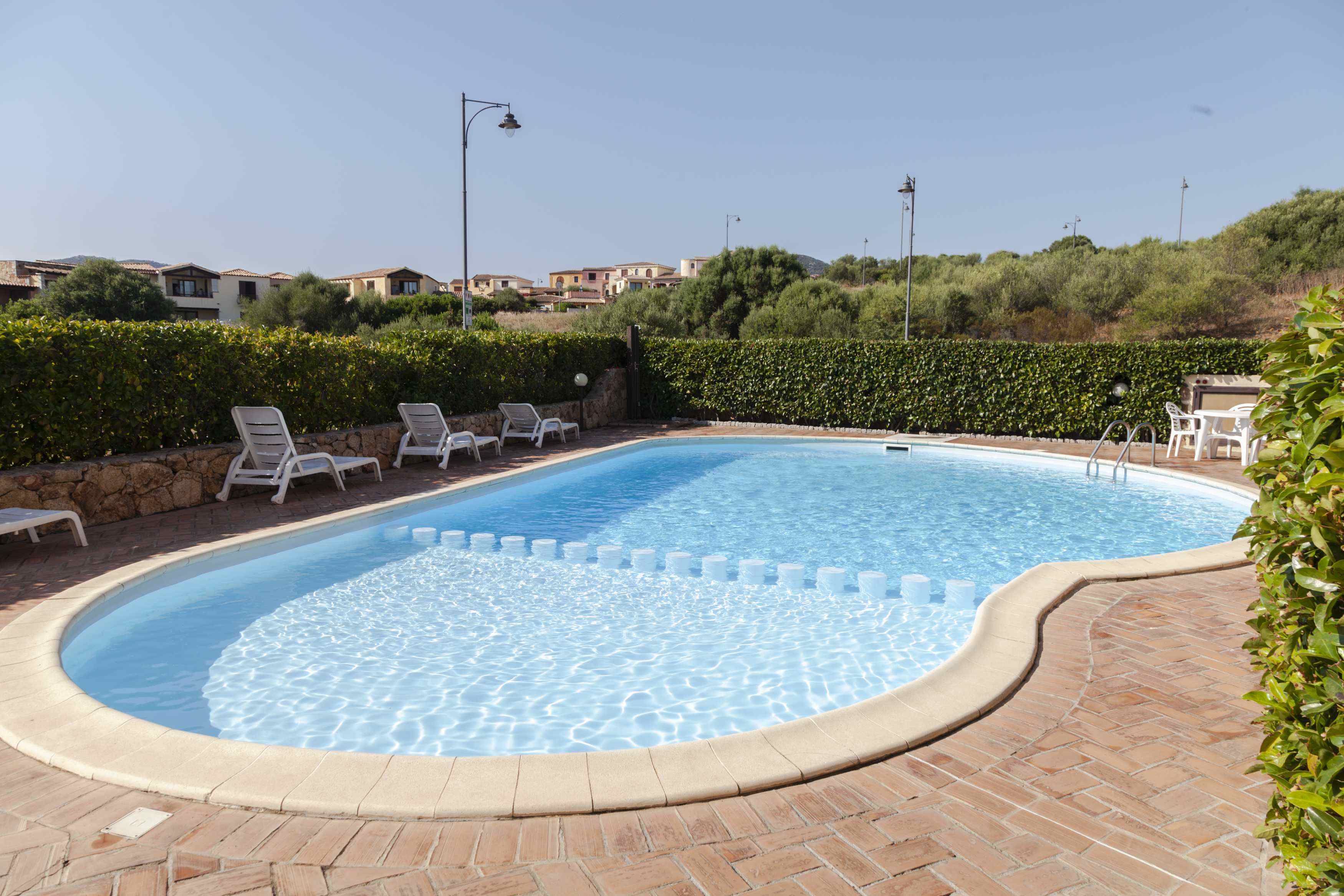 Une piscine entourée de chaises longues blanches et d’une terrasse en briques.