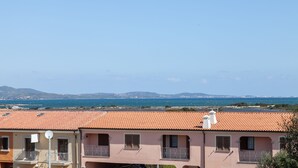 A coastal building with a red-tiled roof, balconies, and a view of the sea and distant mountains. - Aria di vacanza - Borgo Turchese (Olbia)