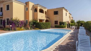 A swimming pool with a brick border, surrounded by white lounge chairs and a building with a beige facade and arched windows. - Aria di vacanza - Borgo Turchese (Olbia)