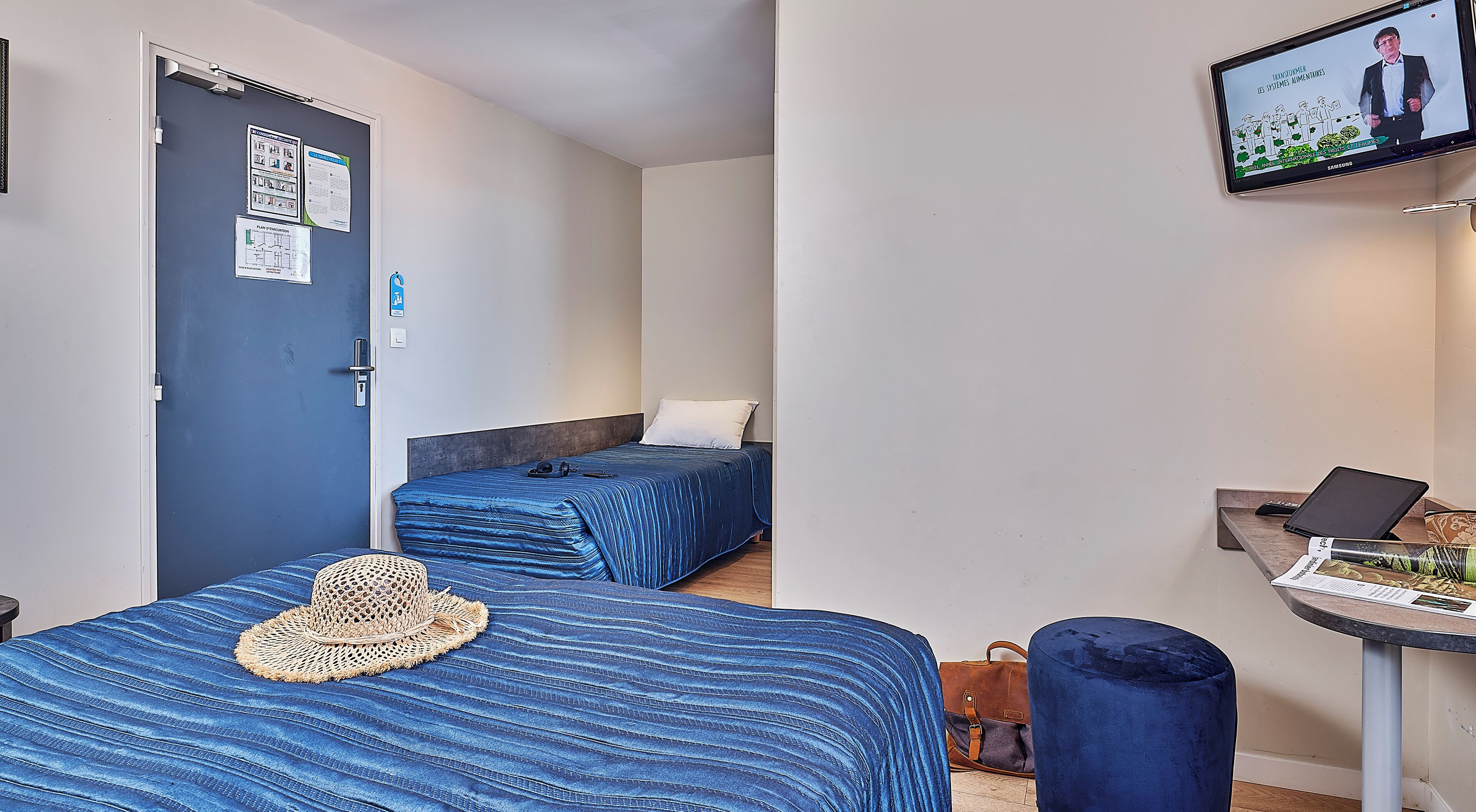 Une petite chambre moderne, équipée de deux lits, d’un bureau et d’une télévision.