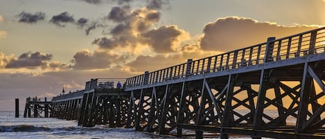 Un muelle que se adentra en el agua con un atardecer de fondo.