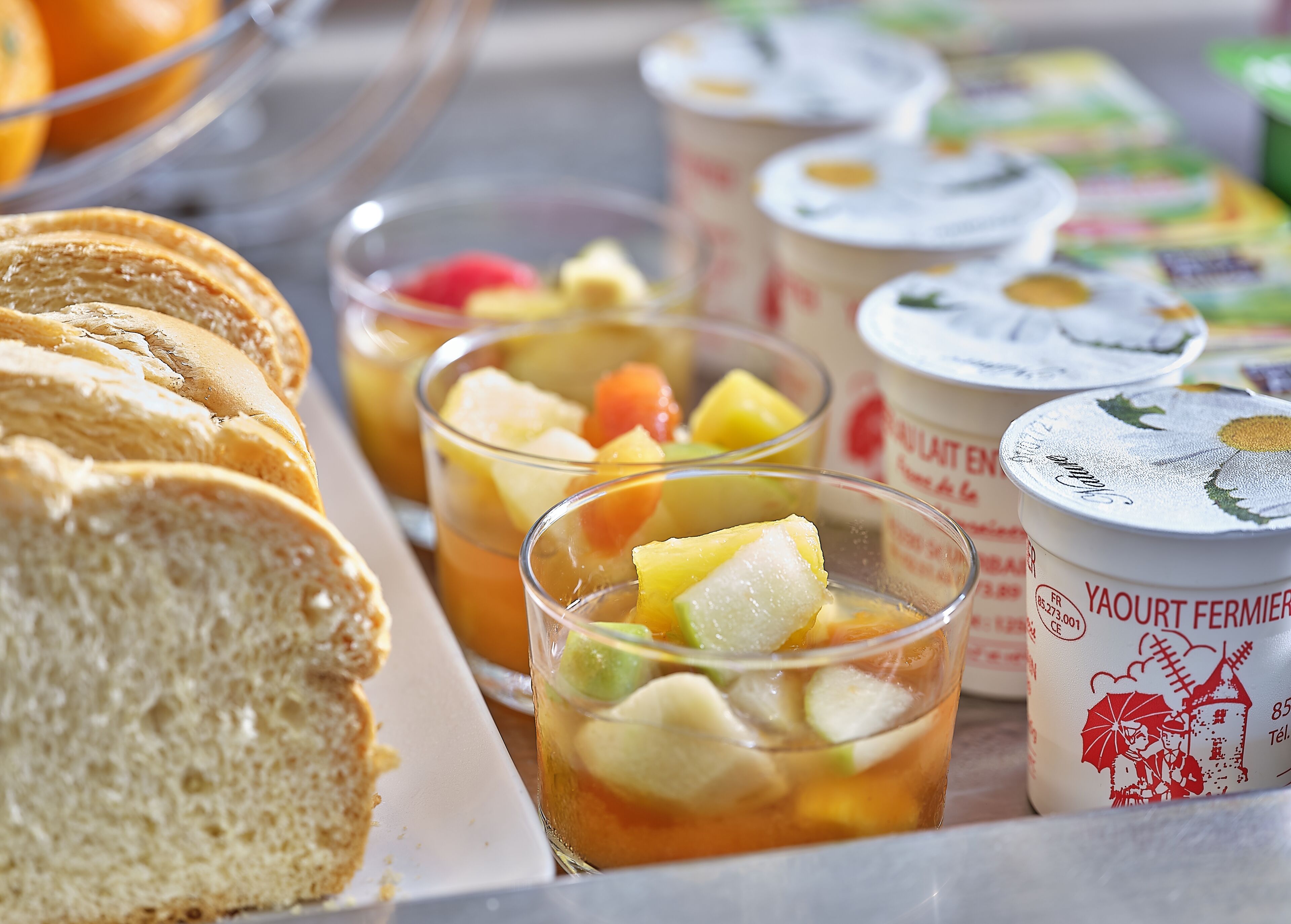 Ein Frühstücksbuffet mit Brot, Obstbechern und Joghurt.