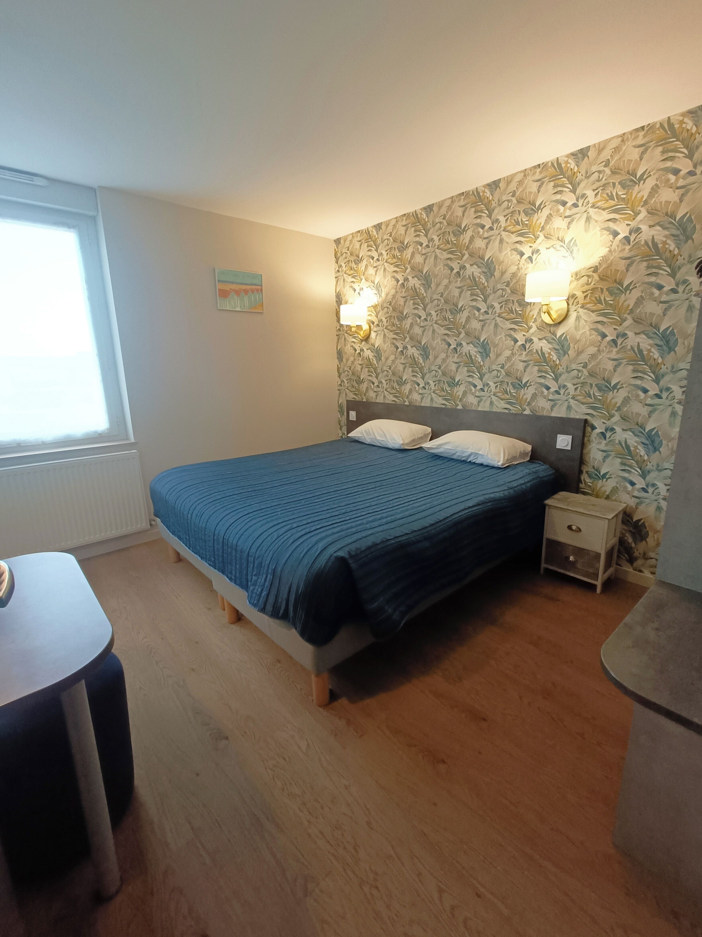 Ein Schlafzimmer mit einem Bett, Nachttischen, einem kleinen Tisch und einem Fenster.