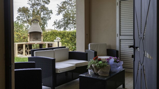 Un espacio de patio con mobiliario de mimbre, una parrilla y una puerta que da al exterior.
