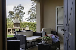 Eine Terrasse mit Korbmöbeln, einem Grill und einer Tür zum Außenbereich.