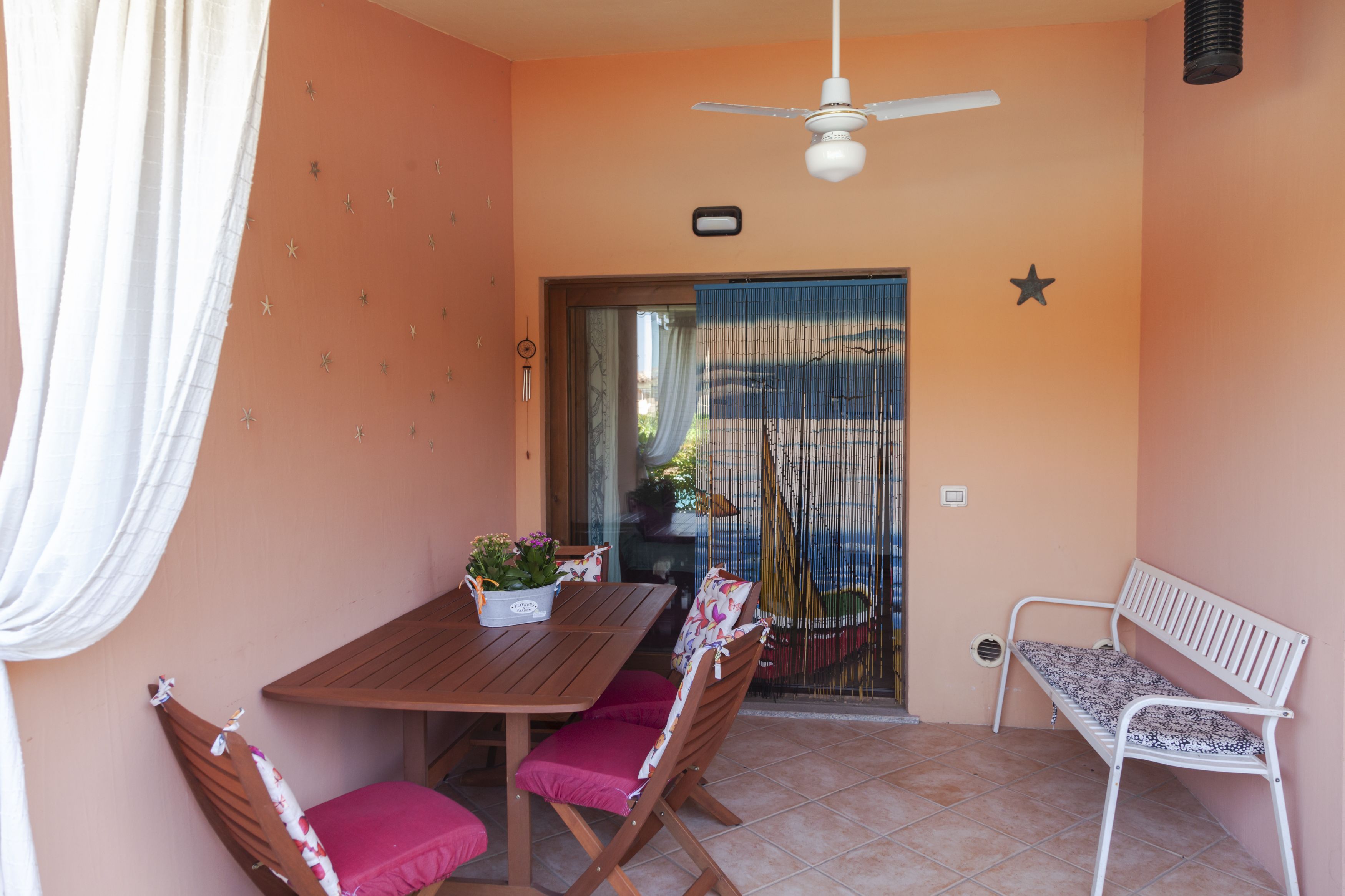 A patio with a wooden table, two chairs, a white bench, and a ceiling fan.