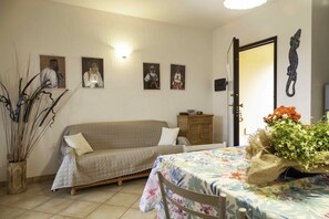 A cozy living room with a sofa, a table with a floral tablecloth, and a cabinet. There are framed pictures on the wall and a decorative wall hanging. - Aria di Vacanza - S'Abba Lughente (Olbia)