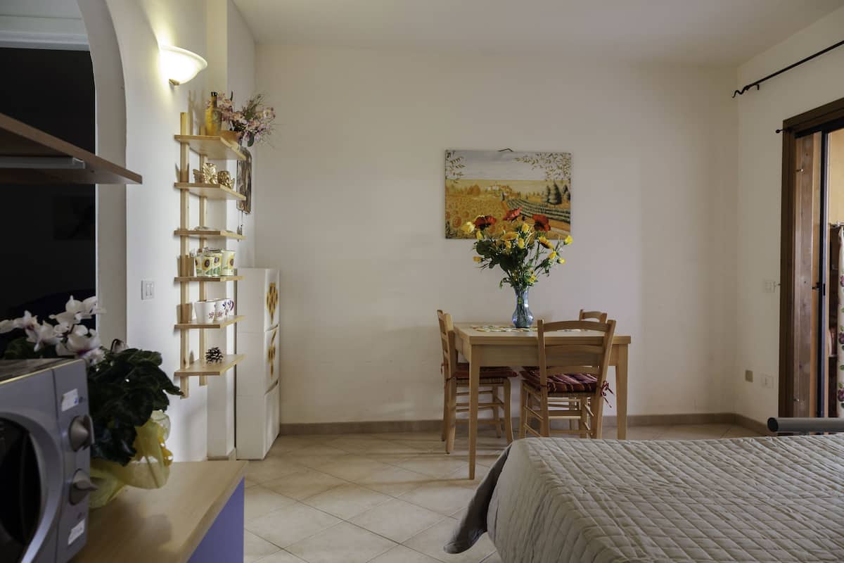 Ein Schlafzimmer mit Bett, Schreibtisch mit Stuhl, Esstisch mit Stühlen, Kühlschrank und einer Wandregal mit Dekoration.