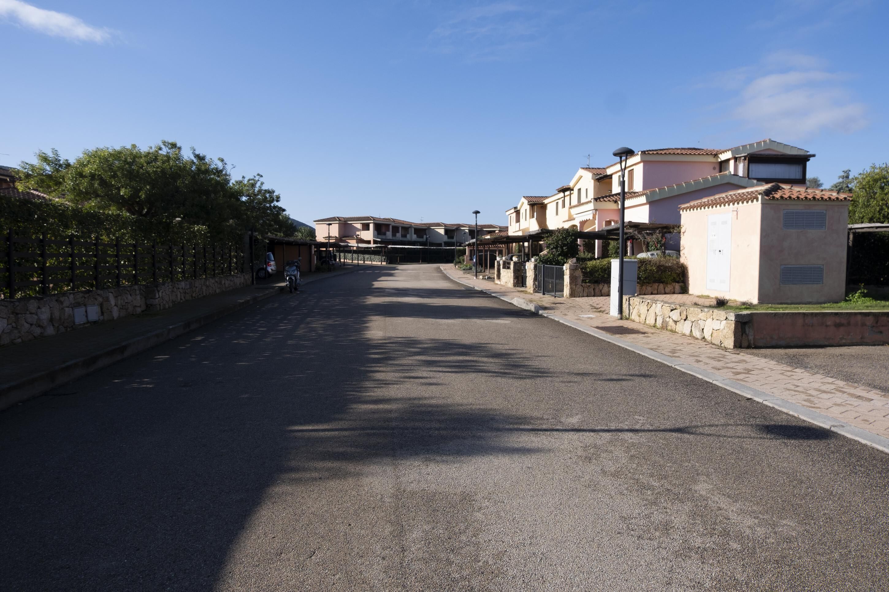A street with buildings, a stone wall, and a clear sky.