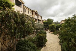A pathway leading to a building with multiple balconies, surrounded by lush greenery and stone walls. - Aria di Vacanza - S'Abba Lughente (Olbia)