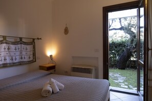 Une chambre à coucher comprenant un lit, un climatiseur fixé au mur, une fenêtre donnant sur un jardin et un élément décoratif mural.