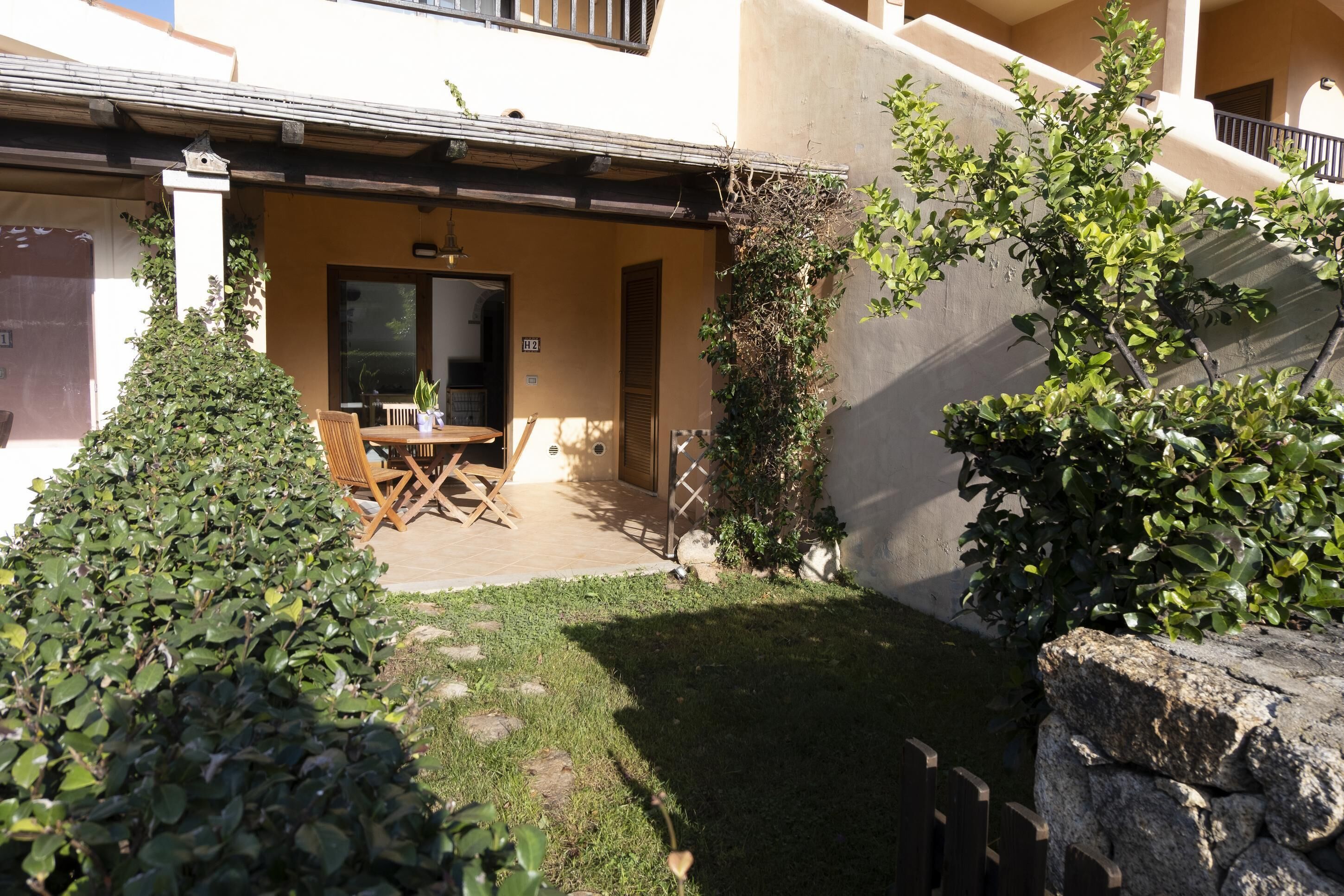 A patio with a table and chairs, surrounded by greenery and a stone wall.