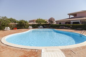 Une piscine dotée d’une terrasse carrelée, entourée d’un jardin aménagé et d’un bâtiment dont le toit est également recouvert de tuiles.