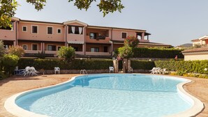 A swimming pool with a tiled deck, surrounded by a low stone wall and a row of white chairs. - Aria di Vacanza - S'Abba Lughente (Olbia)