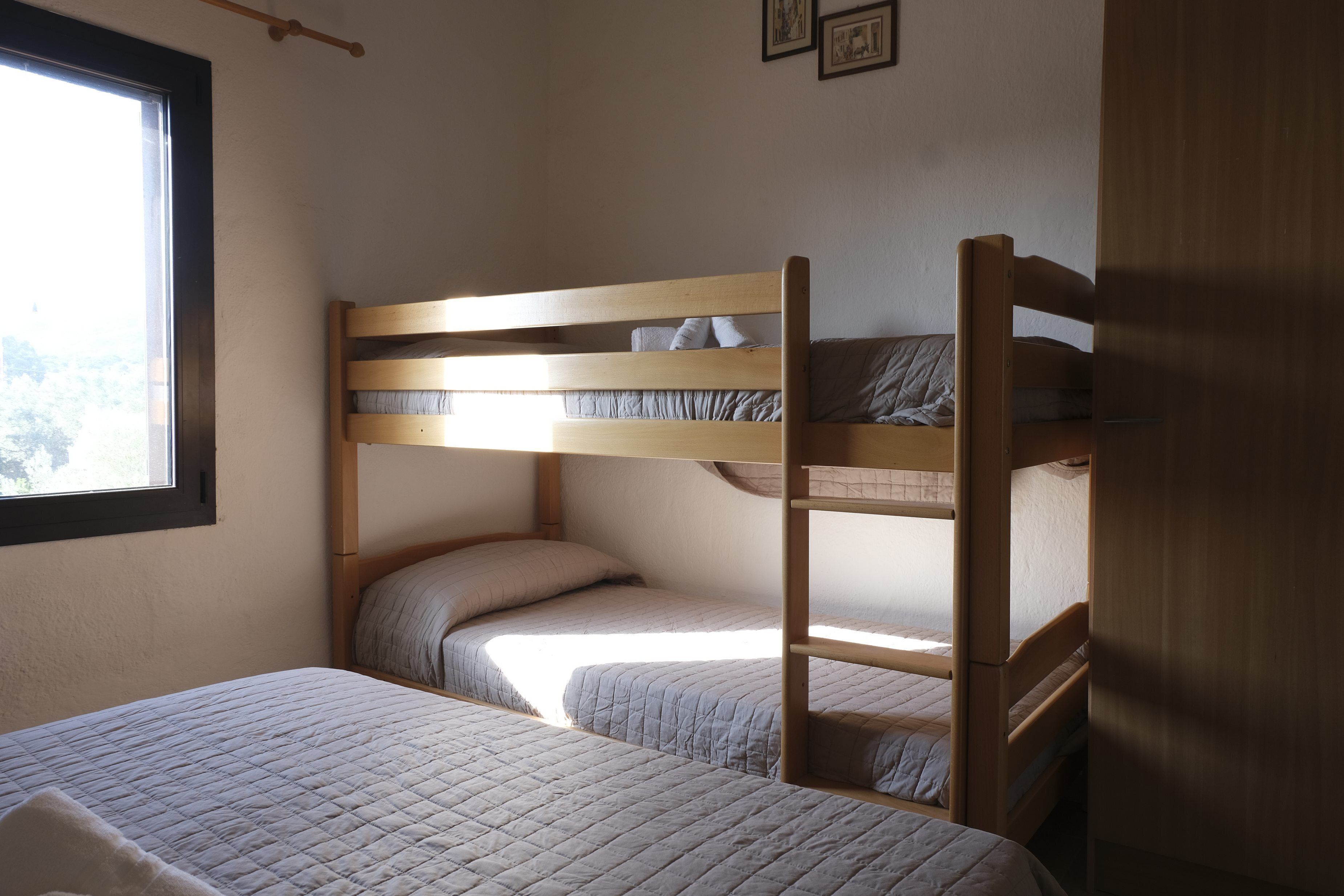 A bunk bed room with a window, wooden headboard, and a bed with a quilted blanket.