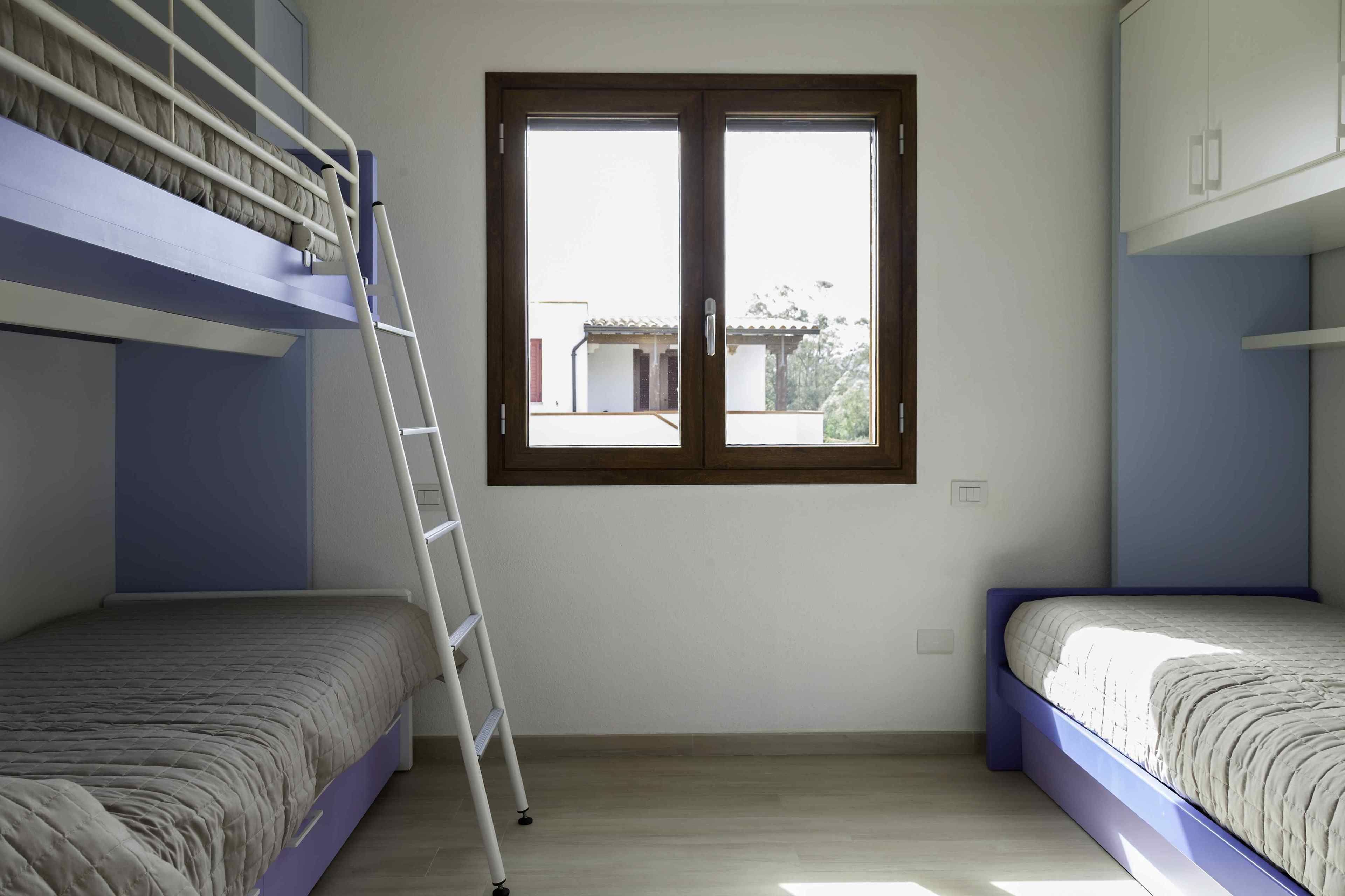 A room with bunk beds, a ladder, and a window with a view of buildings outside.