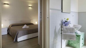Habitación de hotel con cama, mesita de noche, lavabo, espejo y toallero.
