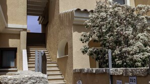 Un edificio con una escalera de piedra que conduce a una entrada, un arbusto de flores blancas y una pared con una puerta y un buzón.