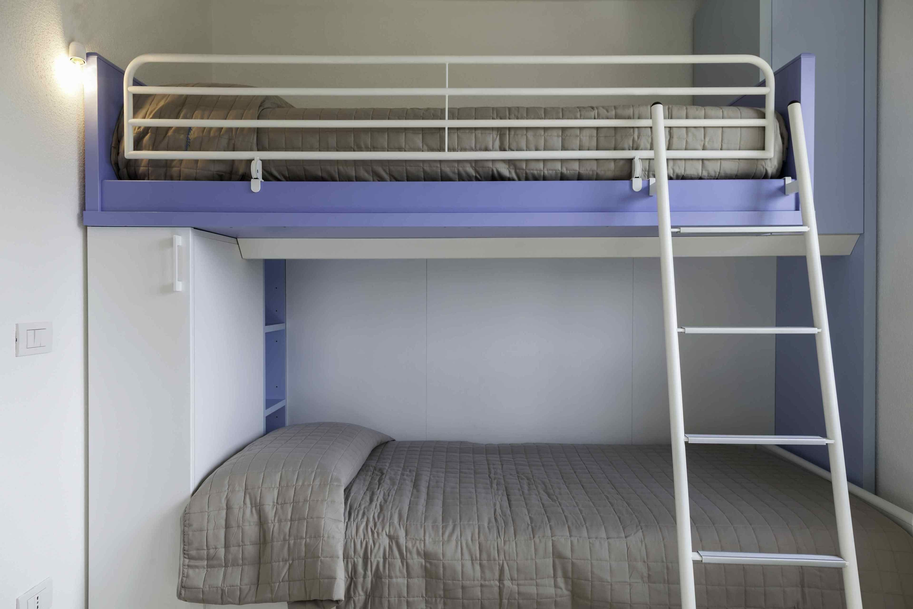 A bunk bed with a ladder, a single bed below, and a wall-mounted shelf.
