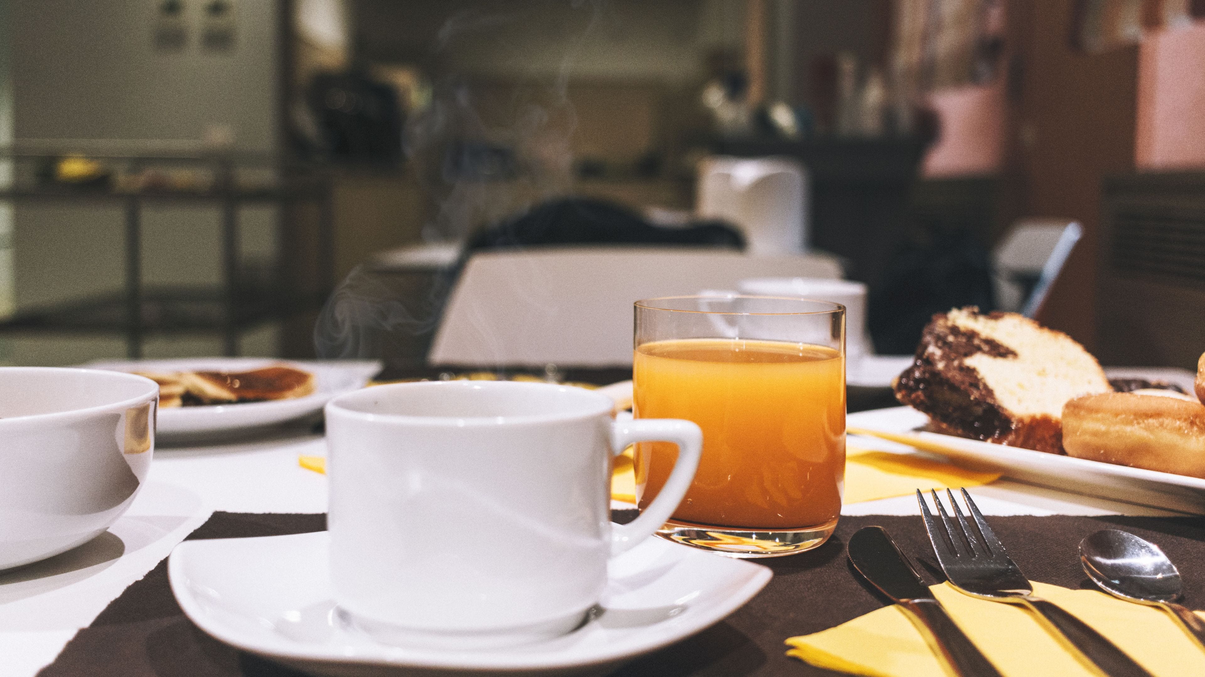 A breakfast setting with a cup of tea, a glass of orange juice, and pastries on a table.