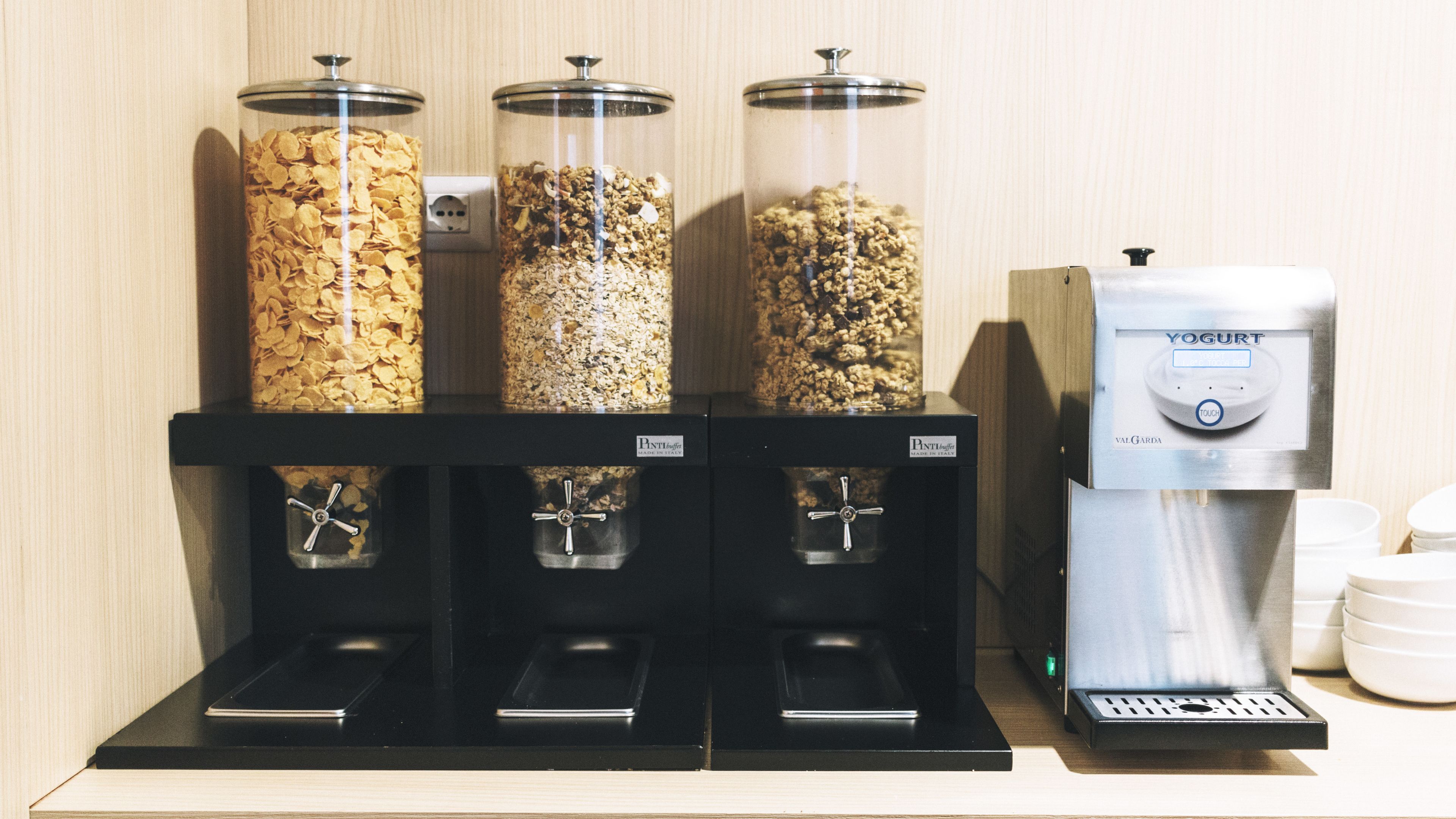 A self-serve station with three dispensers for granola and yogurt, and a coffee machine.
