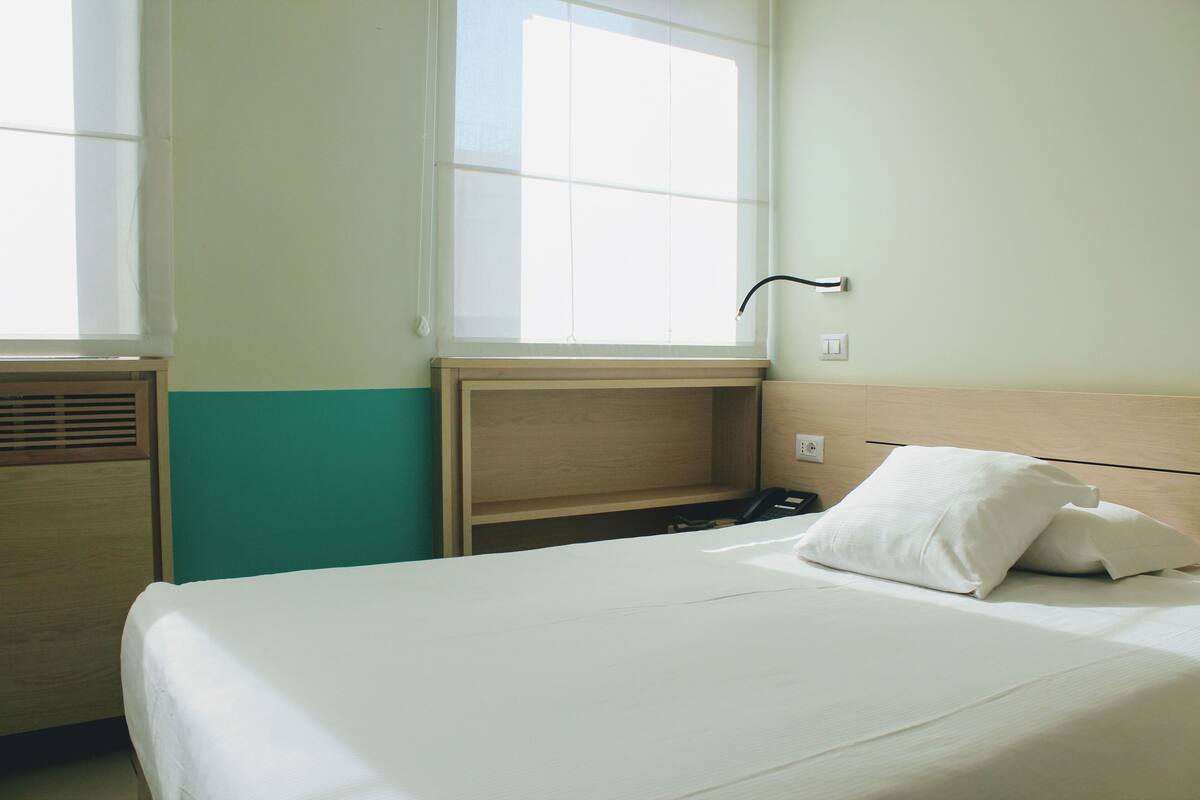Ein Hotelzimmer mit Bett, Fenster, Nachttisch und einer Steckdose.
