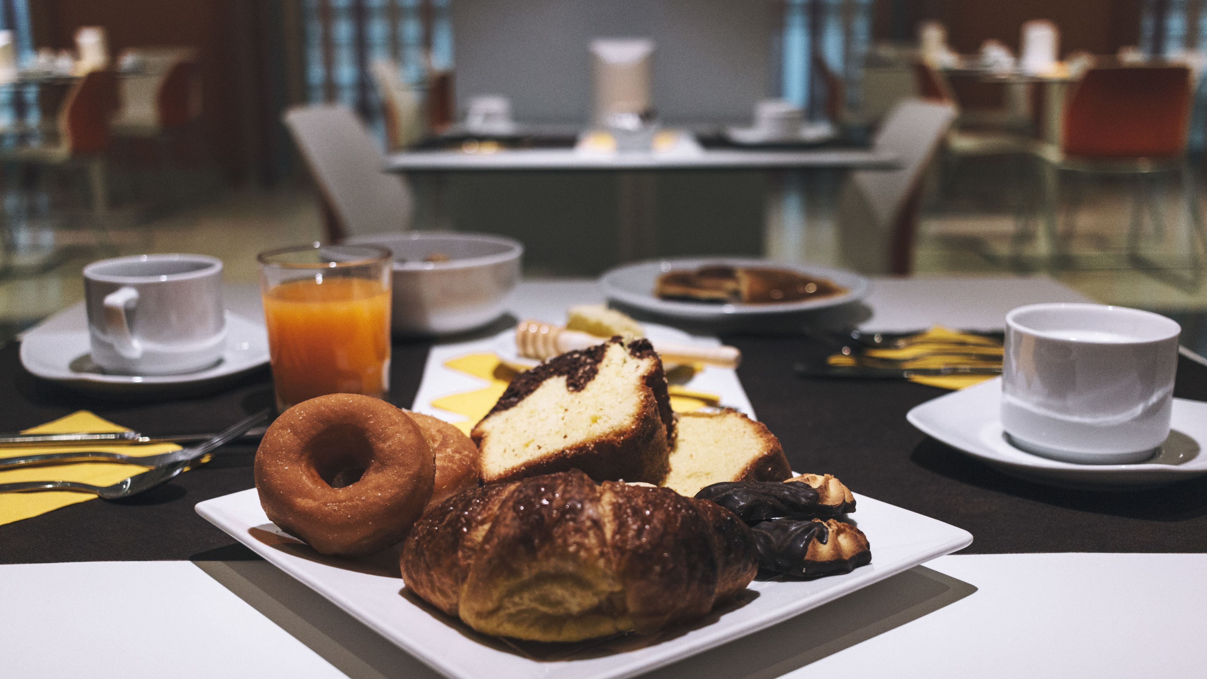 Une table de petit-déjeuner avec des viennoiseries, un verre de jus d’orange et une tasse de café.