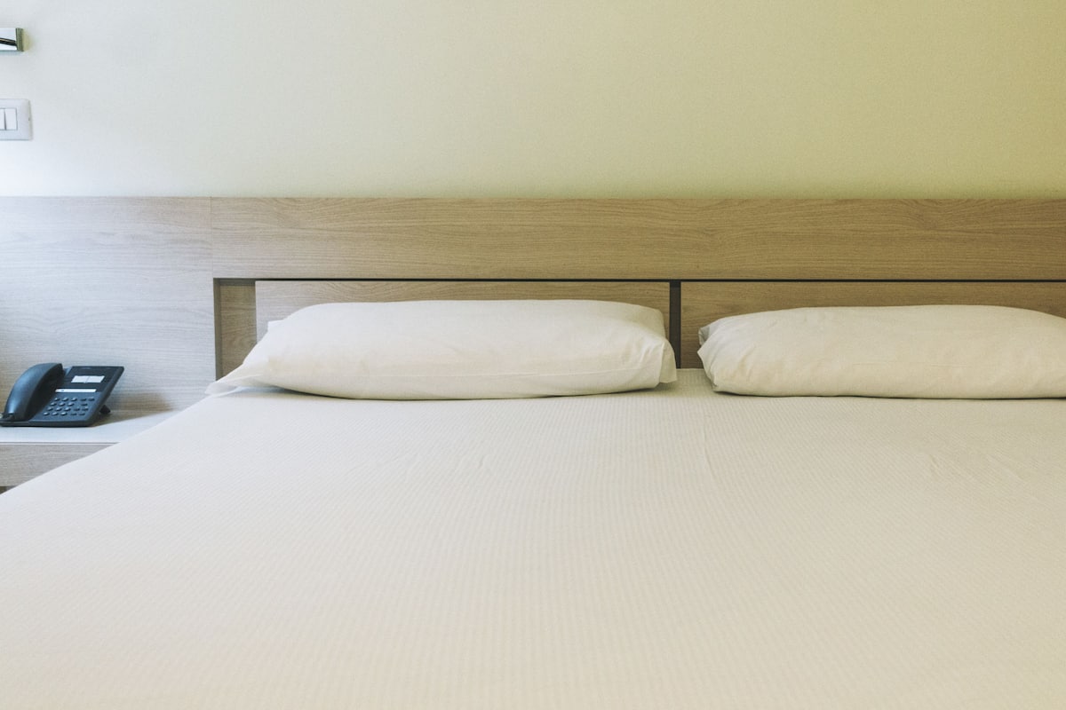 Ein Hotelzimmer mit hölzernem Kopfteil, zwei weißen Kissen und einem Nachttischtelefon.