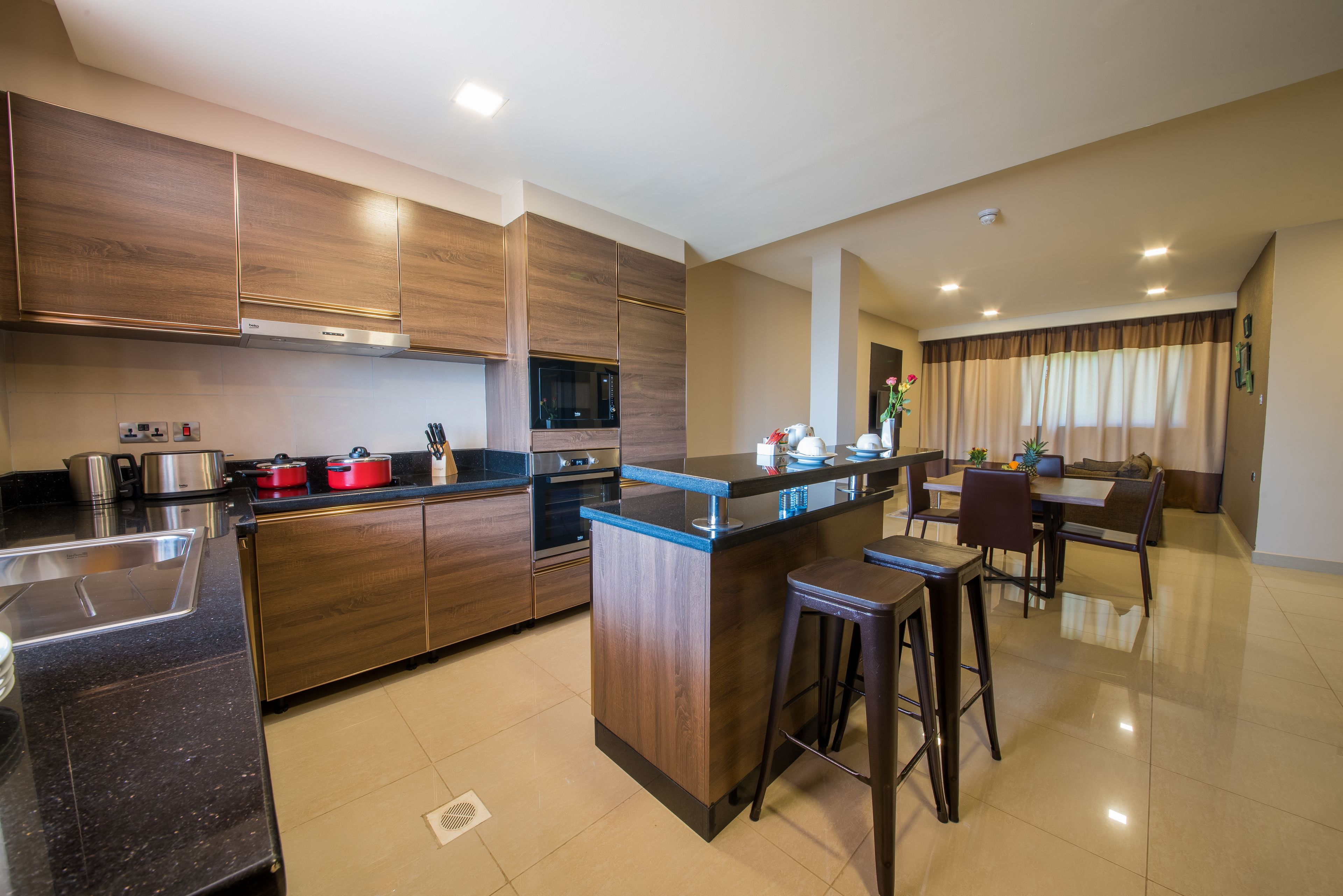 A modern kitchen with wooden cabinets, a central island, bar stools, and a dining area with a table and chairs.