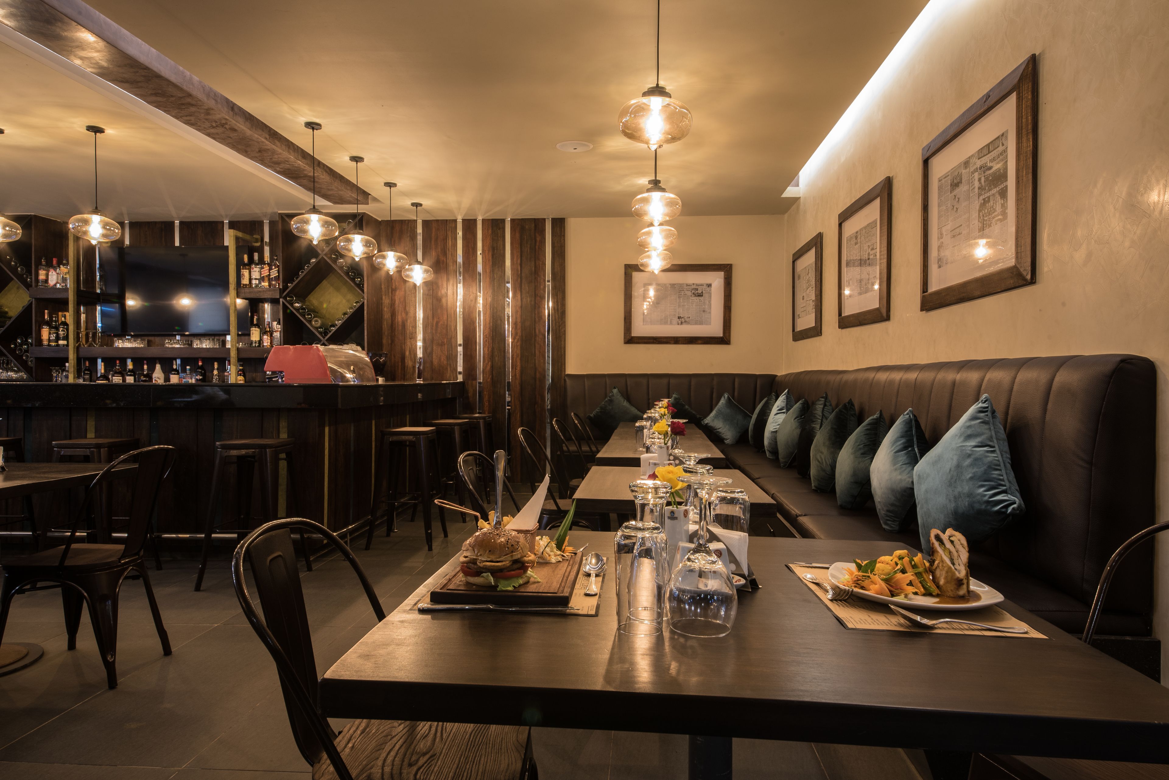 Restaurante com uma mesa comunitária grande, área de bar e assentos acolchoados.