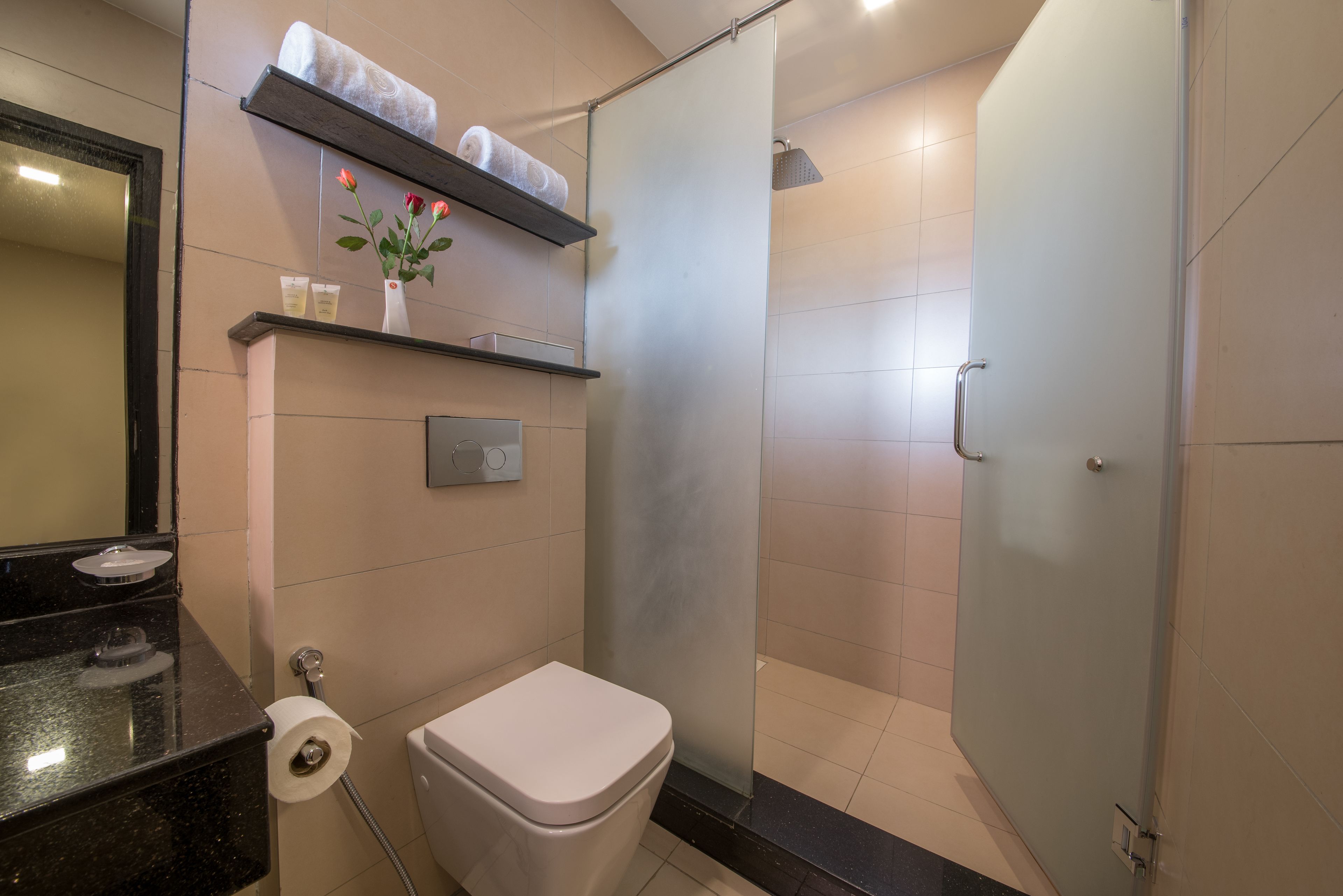 Une salle de bain moderne comprenant des toilettes, une douche, un meuble-lavabo avec un miroir, ainsi que des étagères avec des serviettes et des articles de toilette.