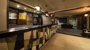 En modern entréhall med en vägg som har ett geometriskt mönster, en receptionsdisk och en sittgrupp med en soffa och ett litet bord.